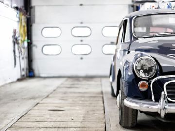 Teilansicht eines dunkelblauen Oldtimers in einer hellen Werkstatt mit geschlossenem Garagentor im Hintergrund – Aufnahme von vorn rechts, Fokus auf Scheinwerfer und Kühlergrill.