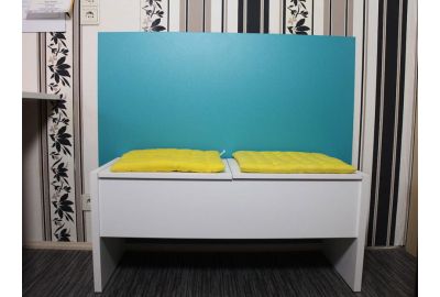 Weiße Sitzbank mit zwei gelben Sitzkissen vor einem türkisfarbenen Wandschutz; im Hintergrund Tapete mit schwarzen und beigefarbenen Streifen und Blumenmustern.