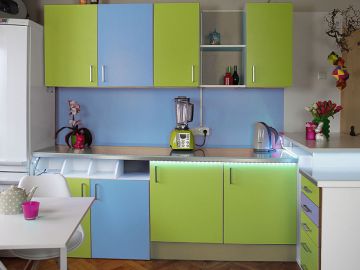 Farbenfrohe Küche mit Ober- und Unterschränken in Hellgrün und Hellblau. Die Küchenfronten und -rückwände wurden mit Wandpaneelen verkleidet. 