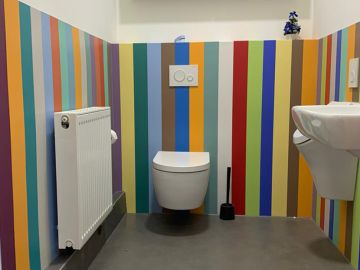 Toilettenraum mit buntem Farbkonzept aus vertikal gestreiften Wandschutzplatten.