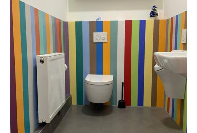 Toilettenraum mit buntem Farbkonzept aus vertikal gestreiften Wandschutzplatten.