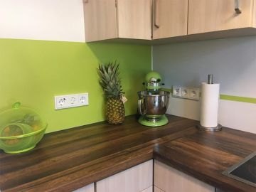 Moderne Küche mit grün abgesetzten Wandpaneel als Rückwand, dunkler Holzarbeitsplatte und hellen Oberschränken.
