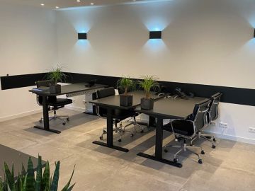 Modern eingerichteter Büroraum mit vier schwarzen Schreibtischen, ergonomischen Bürostühlen, Schreibtischtelefonen und dekorativen Zimmerpflanzen; an der weißen Wand sind schwarze Akzentstreifen aus Wandpaneelen.